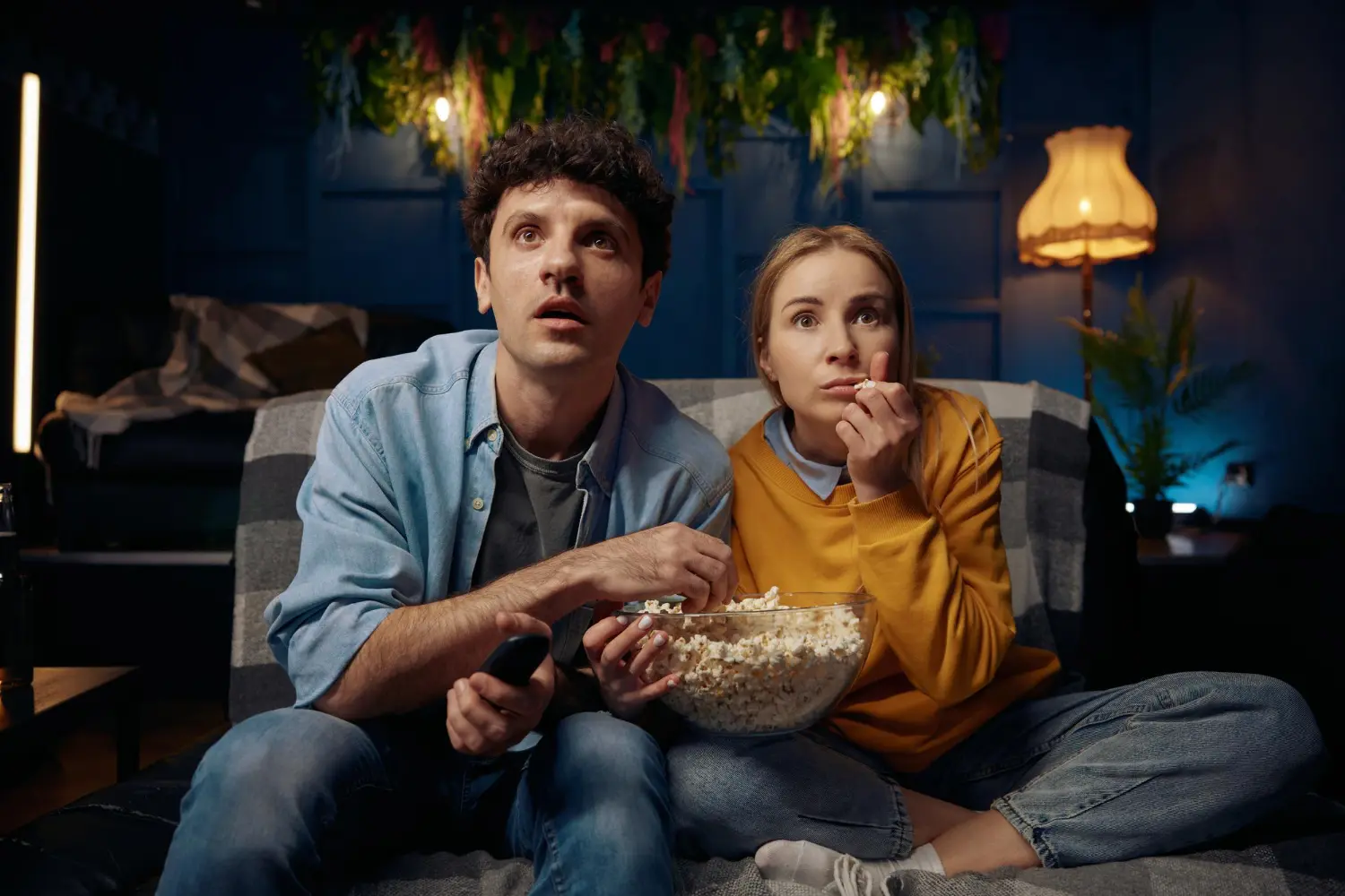 Casal assistindo TV no sofá com expressão de tensão, característica central dos filmes de suspense psicológico.