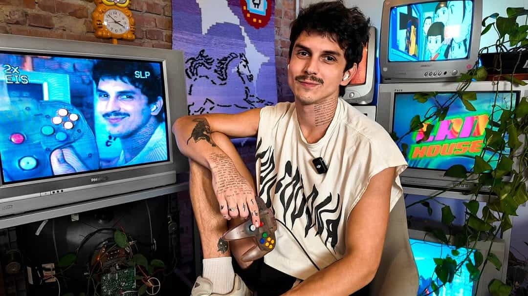 Imagem do Matheus Sodré sorrindo de camiseta branca e uma televisão ao lado.