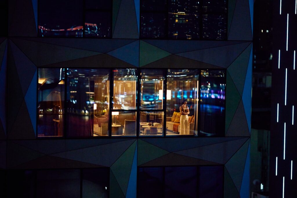 Emmanuelle observa a cidade à noite pela janela de um hotel em cena de Emmanuelle 2025
