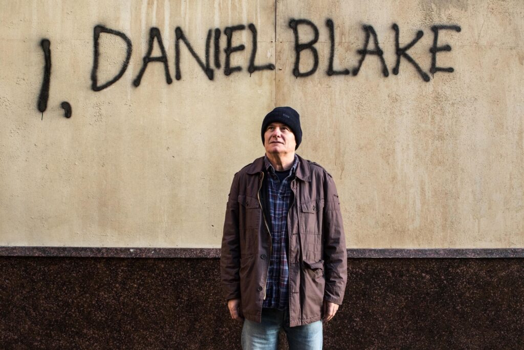 Daniel Blake diante de parede com seu nome escrito em cena do filme Eu, Daniel Blake