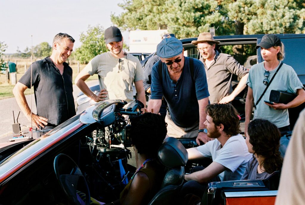 Equipe de filmagem reunida ao redor de carro conversível nos bastidores de Mirrors No. 3