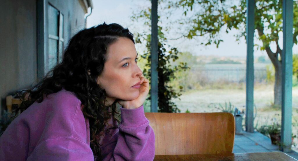 Laura observa a paisagem sentada à mesa em cena de Mirrors No. 3