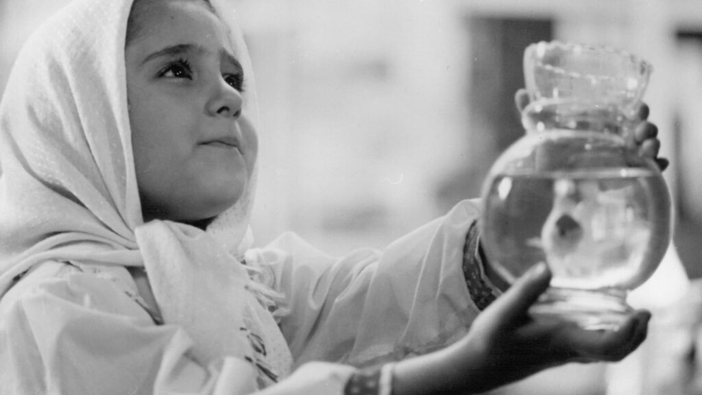 Menina segura um aquário com peixe em cena do filme O Balão Branco
