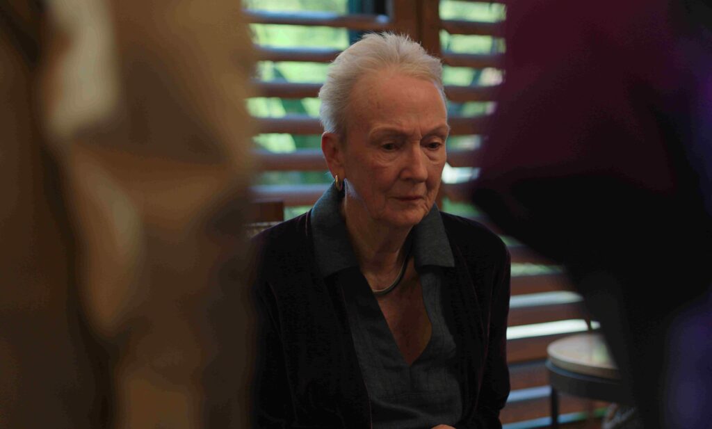Mulher idosa em ambiente interno em cena do filme Toque Familiar